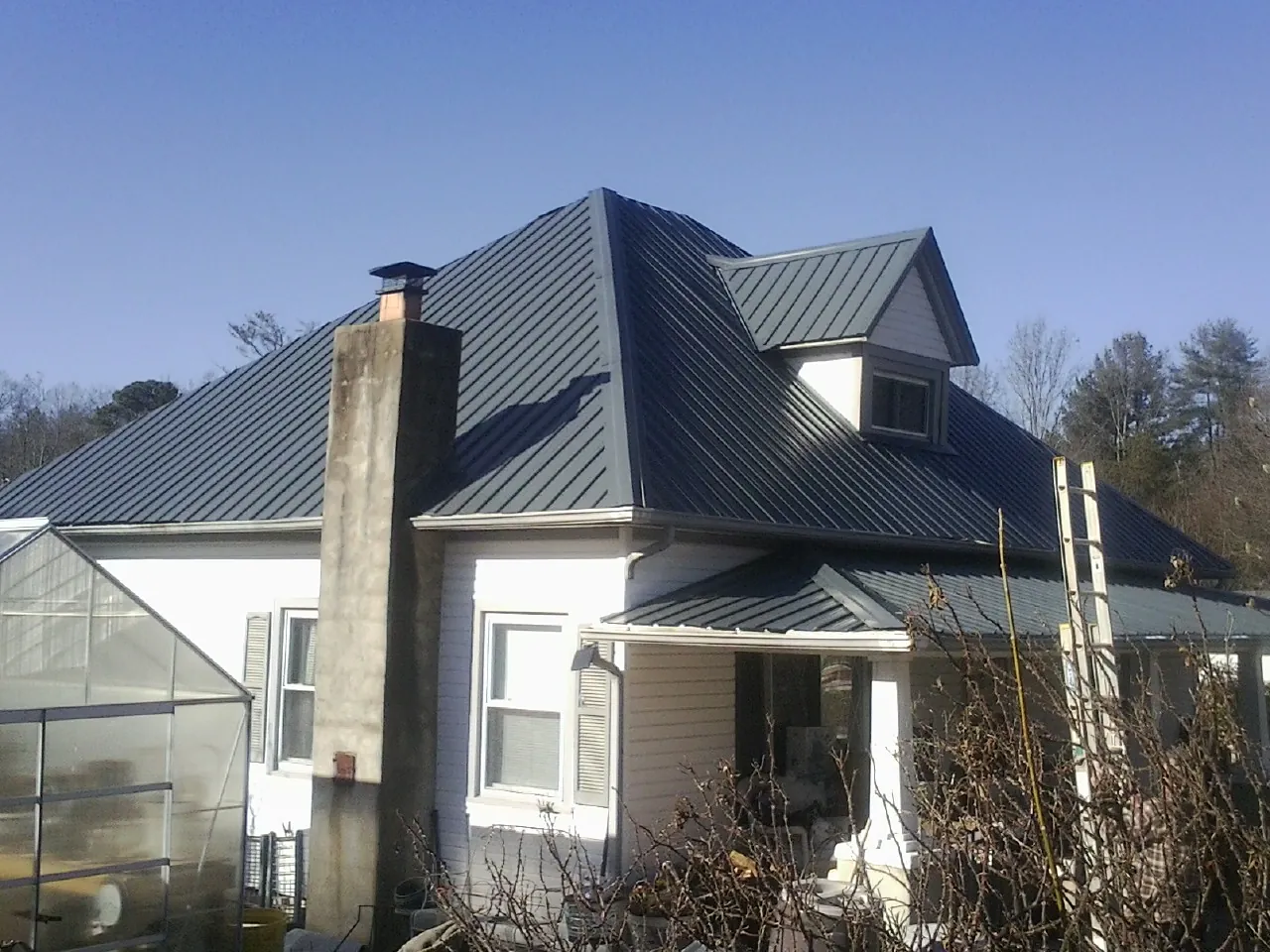 Dark blue standing seam metal roof on a white farmhouse with dormer — Slate & Tile Roof Repair by Roofing Brothers in Newtonville