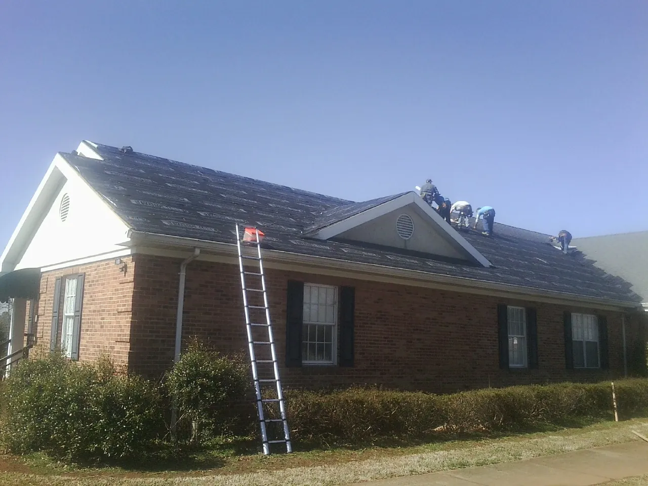 Crew tearing shingles off a brick ranch roof with a ladder set — Emergency Roof Repair work by our crew in Newtonville