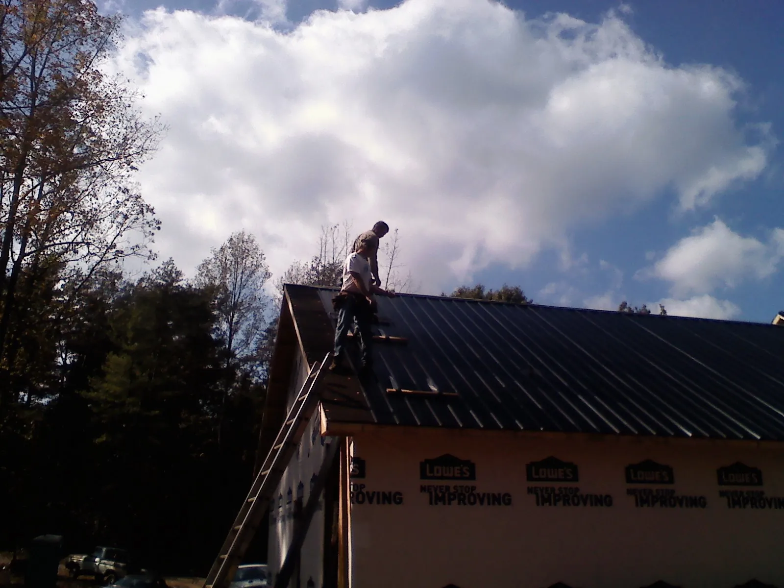 Roofer fastening dark metal panels high against a cloudy sky, from a Roof Inspection job in Newtonville