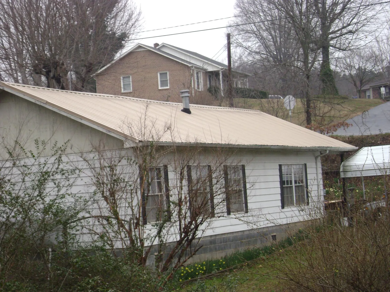 Tan metal roof on a white sided house set into a hillside — Commercial Roofing by Roofing Brothers in Newtonville